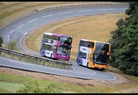 Two, multi-coloured, double-decker buses on a windy road