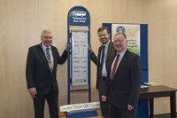 Three men standing with bus stop prototype at launch